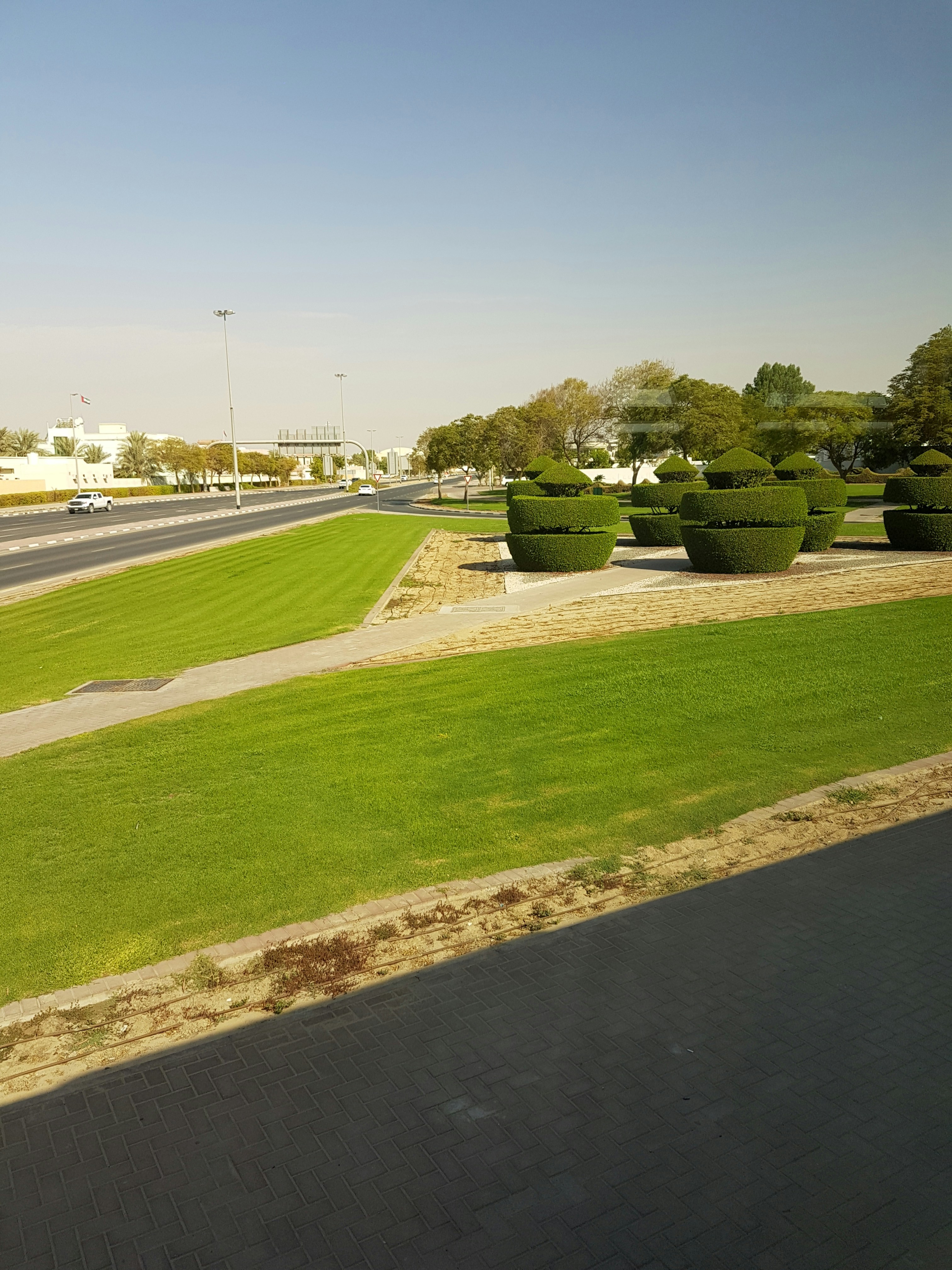 Neat landscaped yard with trimmed green grass, clean concrete path, and tidy flower beds on a clear day