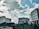 Several modern office buildings are positioned against a backdrop of a partly cloudy sky. The architectural structures are surrounded by greenery, including a well-maintained lawn and various plants, adding to the urban landscape.