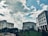 Several modern office buildings are positioned against a backdrop of a partly cloudy sky. The architectural structures are surrounded by greenery, including a well-maintained lawn and various plants, adding to the urban landscape.