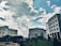 Several modern office buildings are positioned against a backdrop of a partly cloudy sky. The architectural structures are surrounded by greenery, including a well-maintained lawn and various plants, adding to the urban landscape.