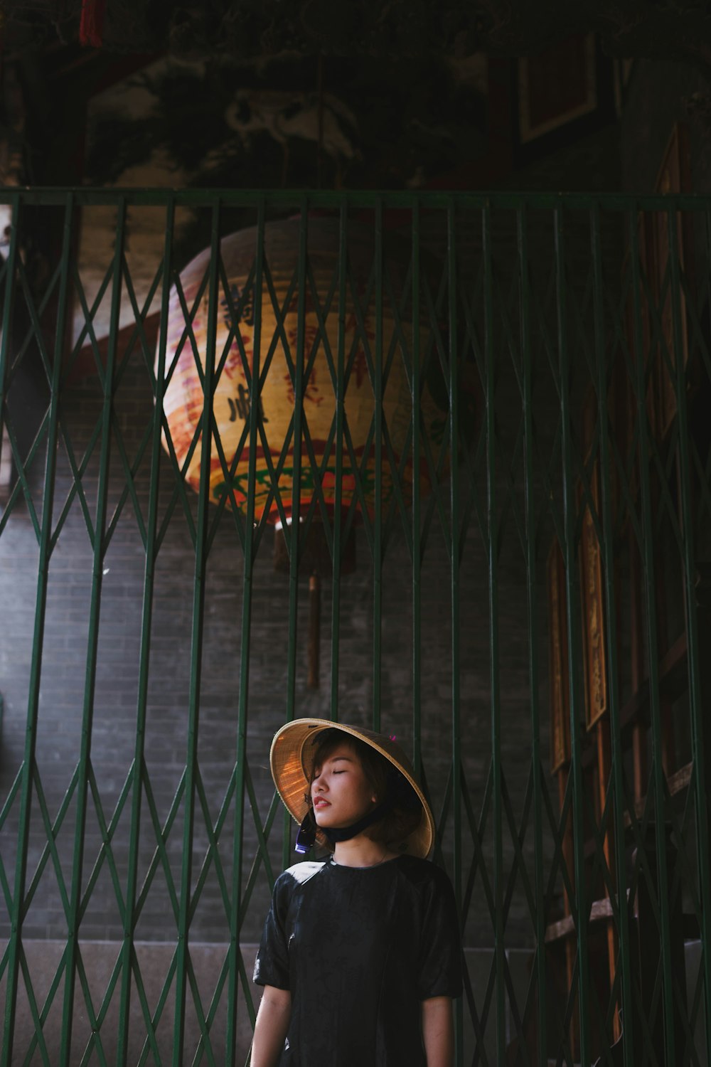 Mujer con sombrero de bambú marrón de pie cerca de la puerta de metal