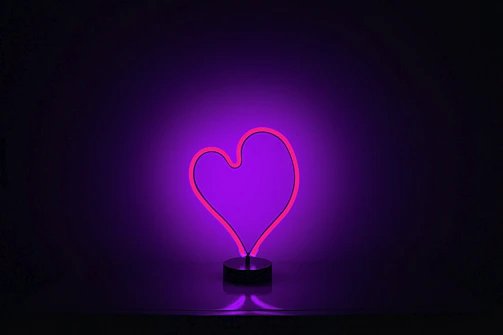 A glowing neon heart made of abstract tiles illuminating a dark background.