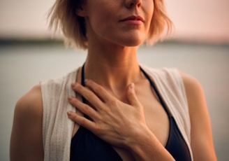 woman in white vest and black bikini with hand on chest