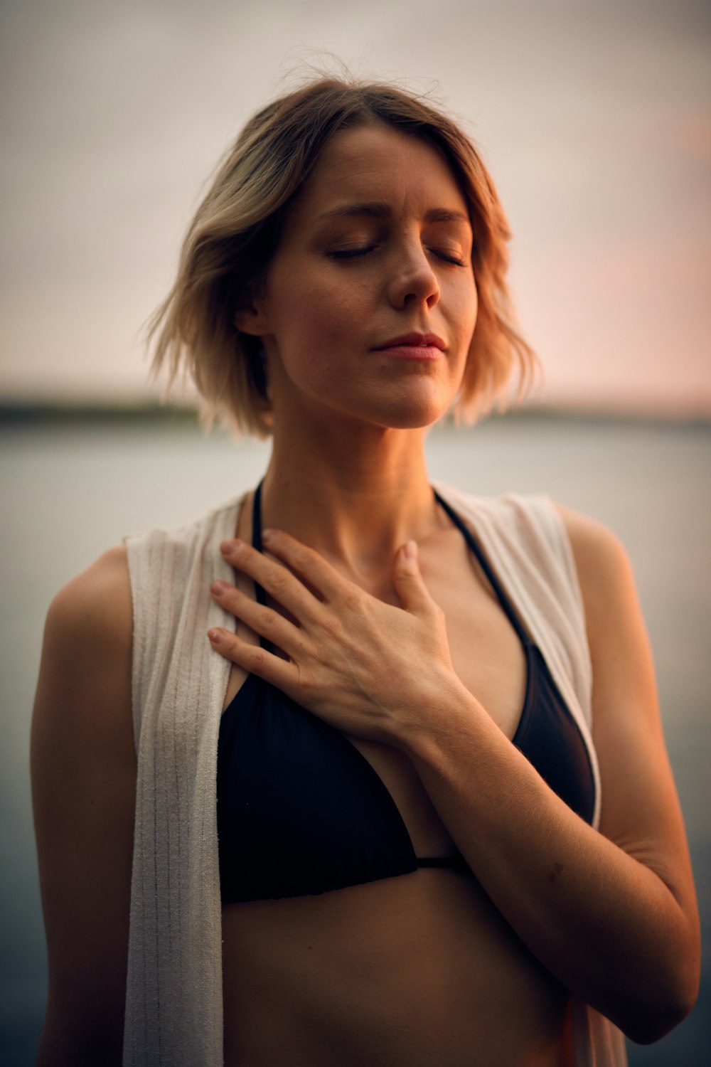 donna in gilet bianco e bikini nero con mano sul petto