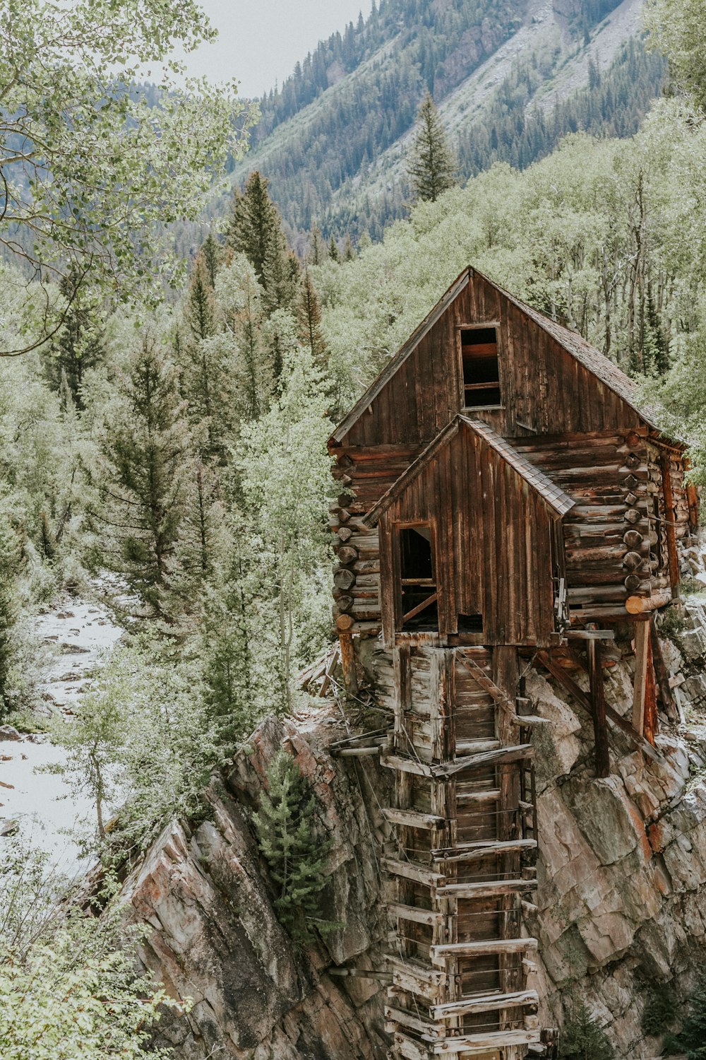 brown wooden house on rock formation near green trees during daytime