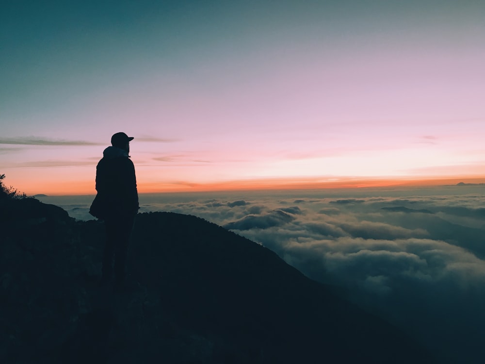 silhouette dell'uomo sulla collina di fronte all'orizzonte con il cielo arancione