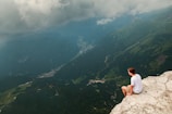 A rider pausing on a cliffside overlook, gazing at a vast valley dotted with winding routes.