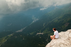 A rider pausing on a cliffside overlook, gazing at a vast valley dotted with winding routes.