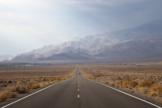 asphalt road going to mountain between grass field in Death Valley National Park United States