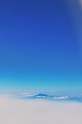 A serene mountain landscape under a clear blue sky with fluffy clouds.