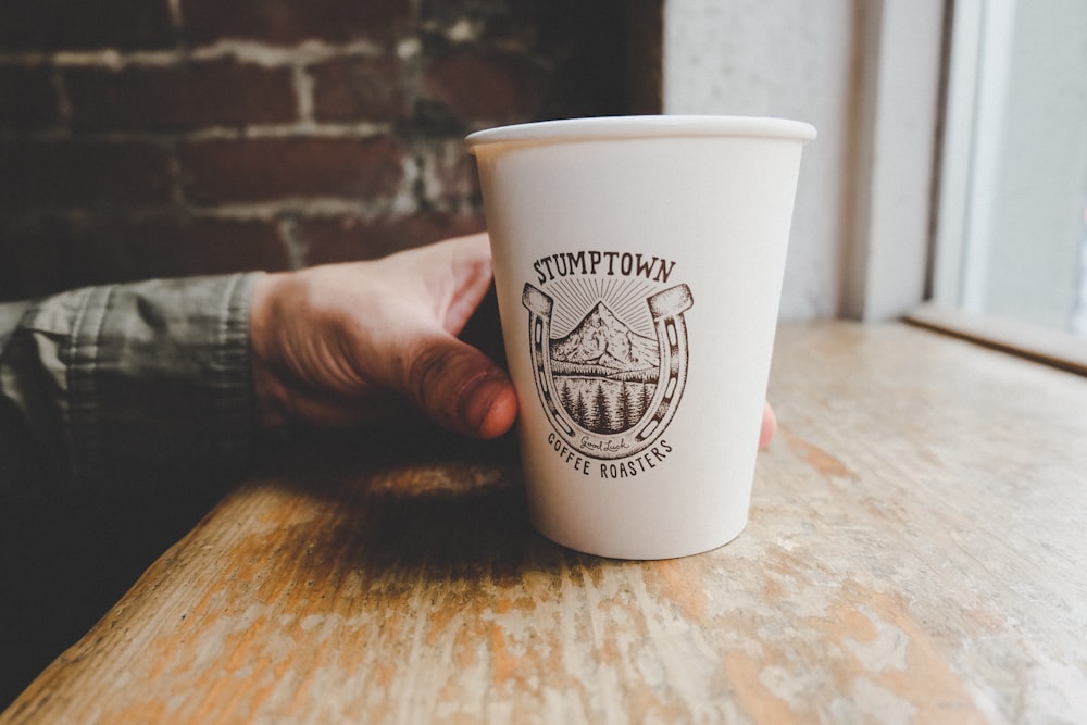 person holding white disposable paper cup