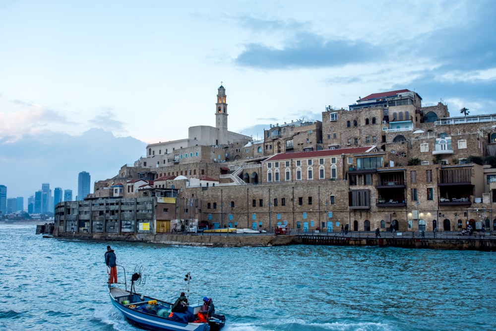 Tre persone che guidano su un motoscafo blu vicino a edifici marroni durante il giorno