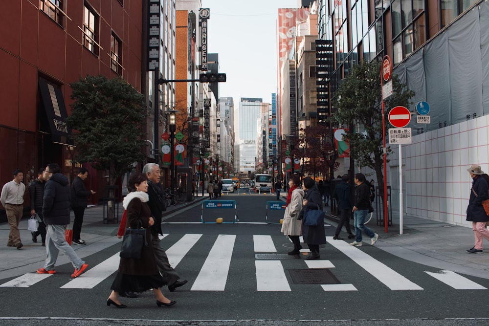 people crossing on road between buildings during daytime