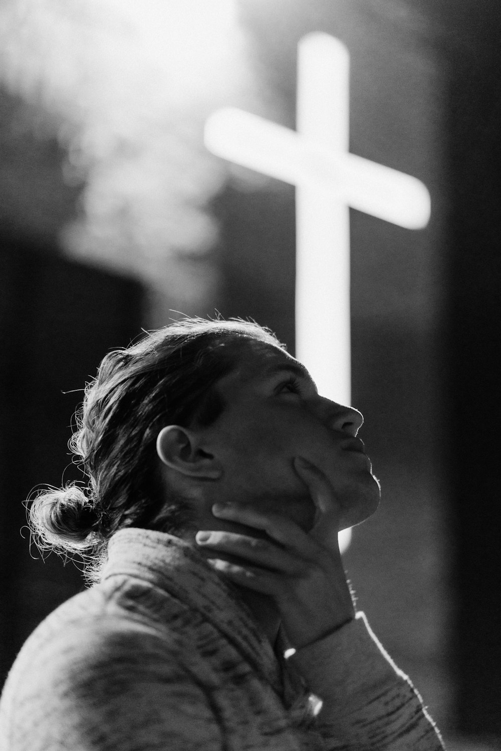 grayscale photography of woman standing near white cross signage