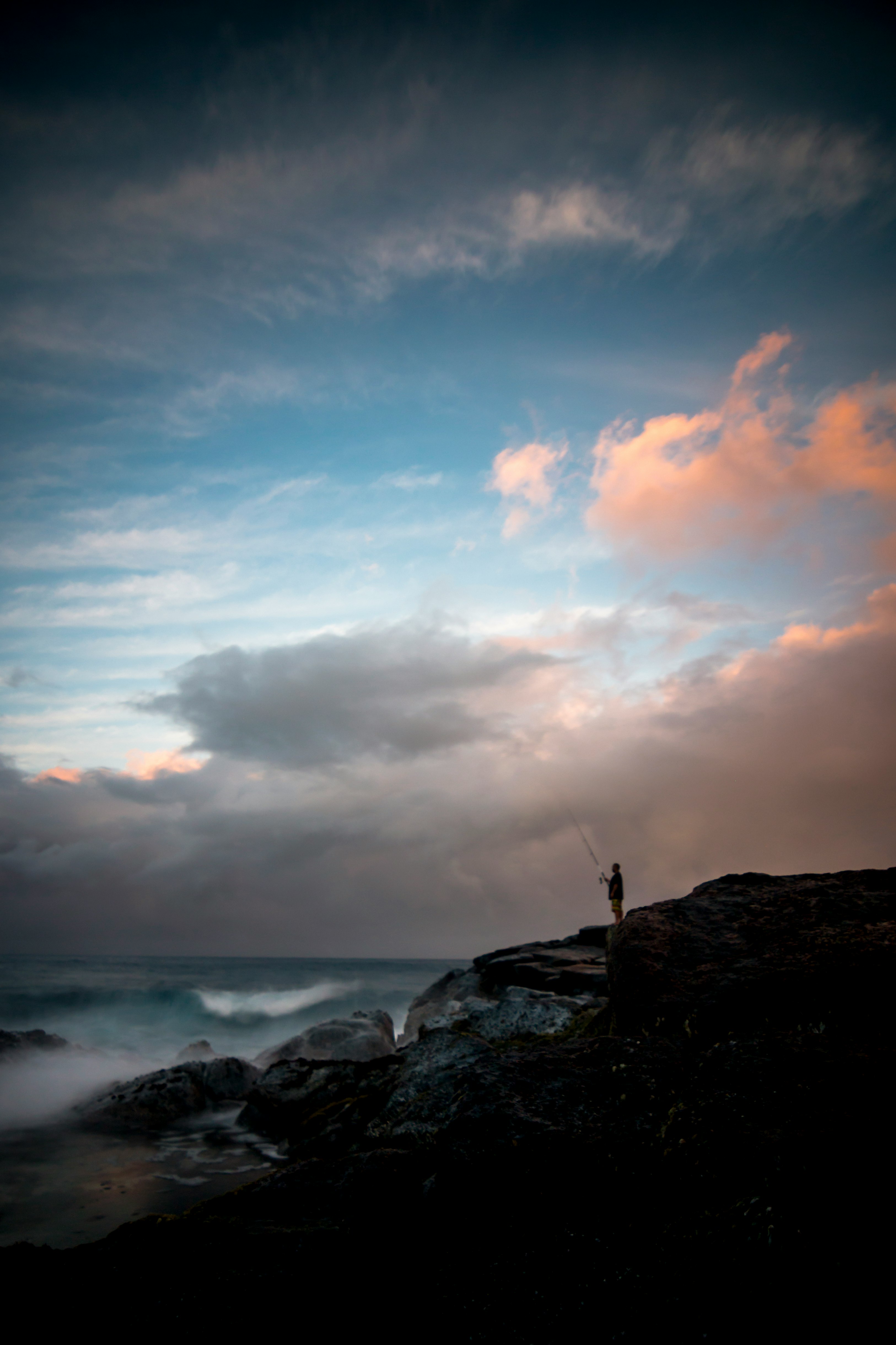 man standing on cliff fishing during daytime