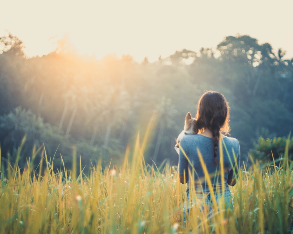 girl carrying dog while standing on grass field