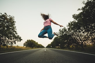 woman in pink top and blue pants jumps on road
