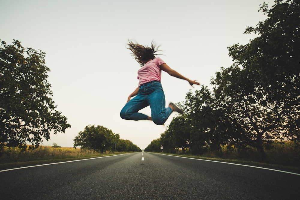 woman in pink top and blue pants jumps on road