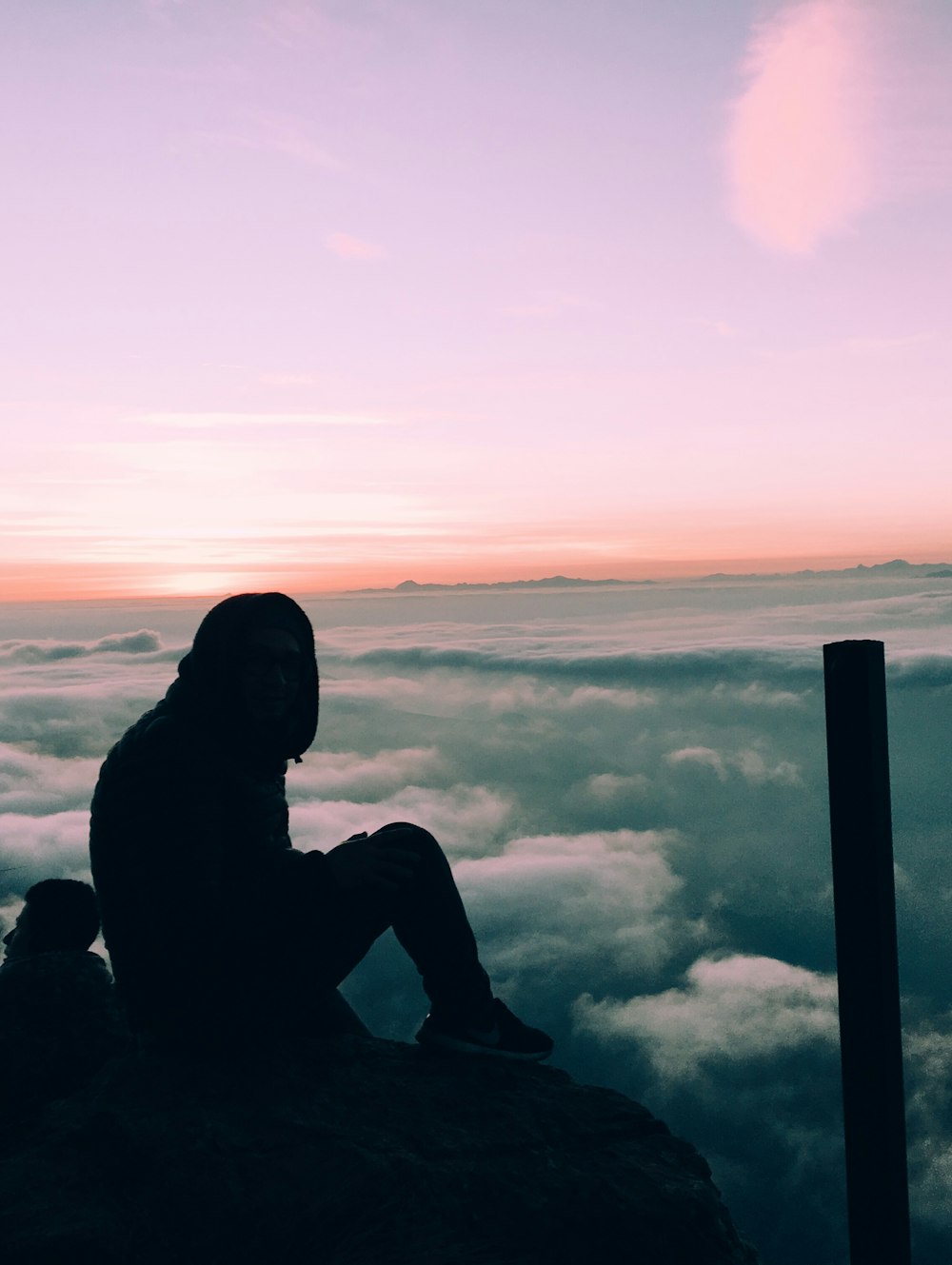 silueta de persona sentada en el acantilado viendo el mar de nubes