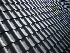 A pattern of dark grey roof tiles with sharp shadows in bright light