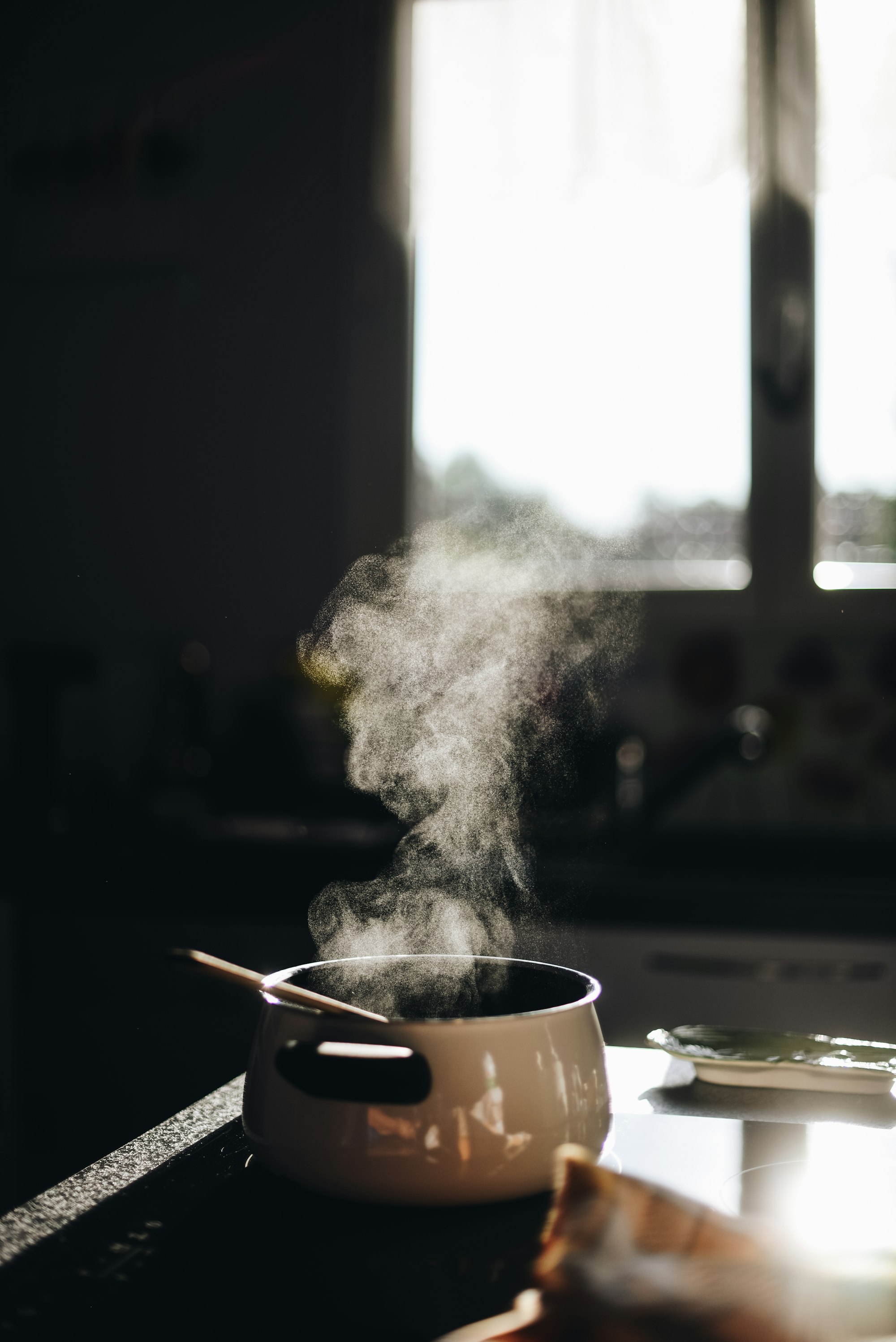 Ein dampender Kochtopf ohne Deckel steht auf einem Herd in halbdunkler Küche