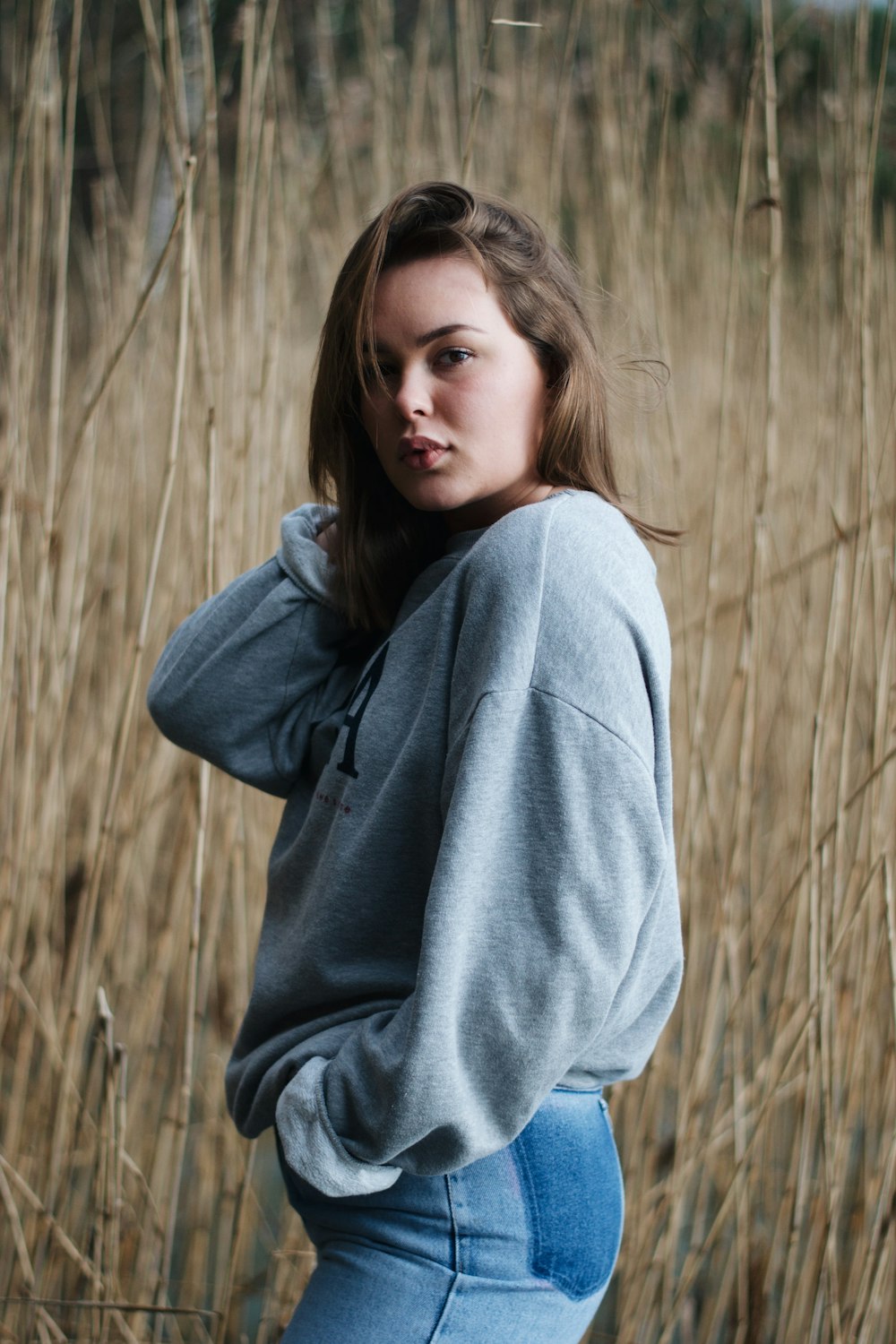 woman in gray long-sleeved shirt and blue denim bottoms standing beside brown field