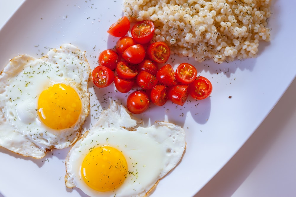 Due uova Sunny Side con pomodori a fette su piatto di ceramica