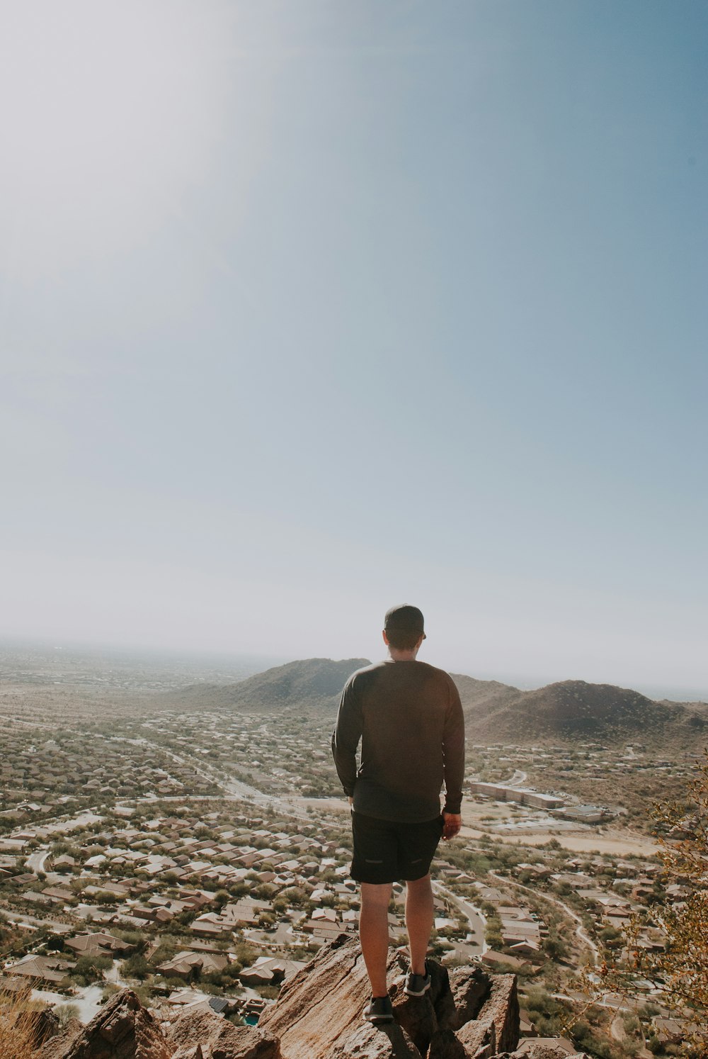 man standing on brown cliff overlooking houses under blue sky during daytime