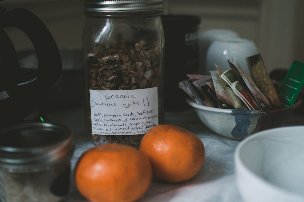 two orange fruits beside Granola labeled clear glass jar