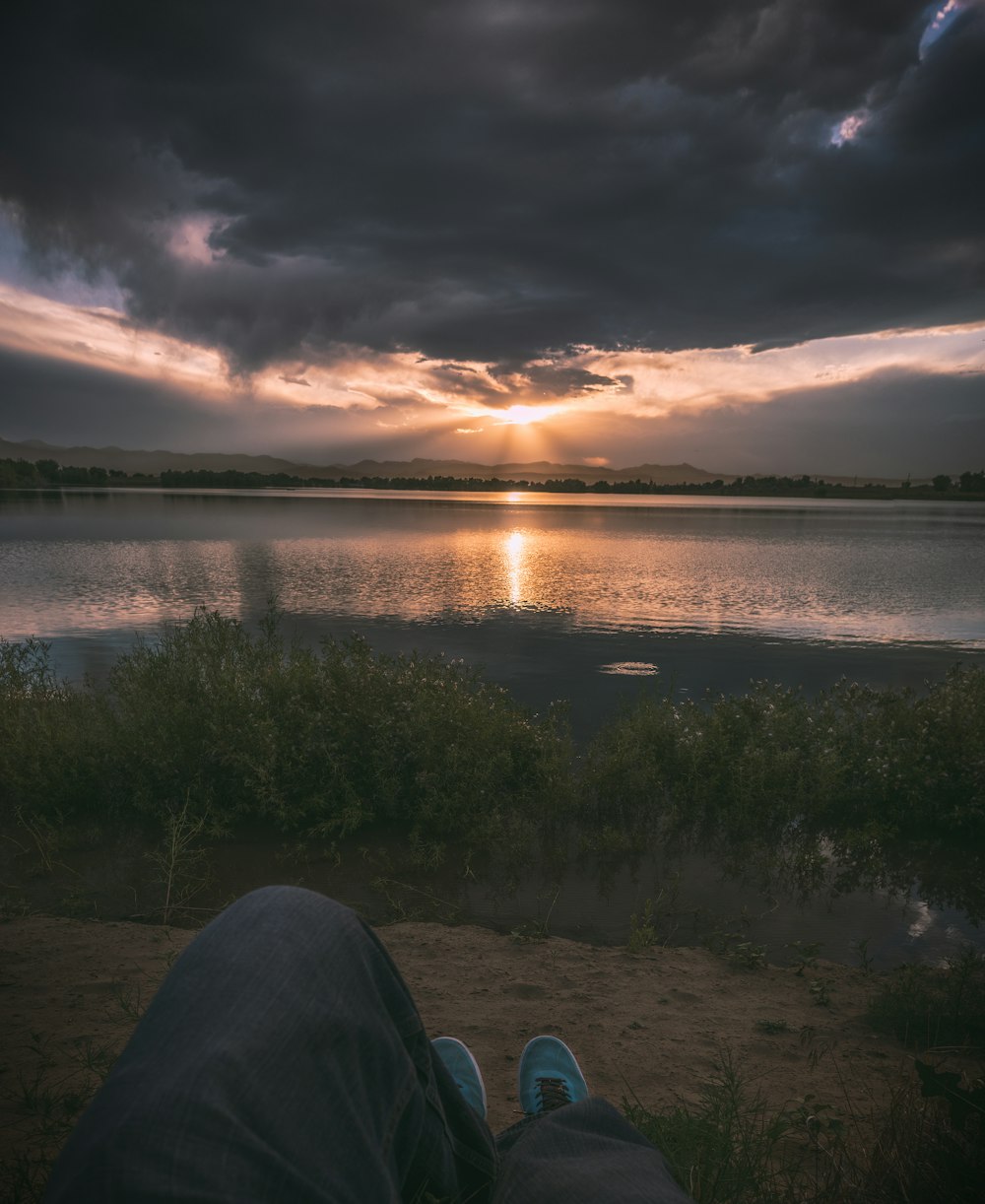 person sitting near body of water during golden hour