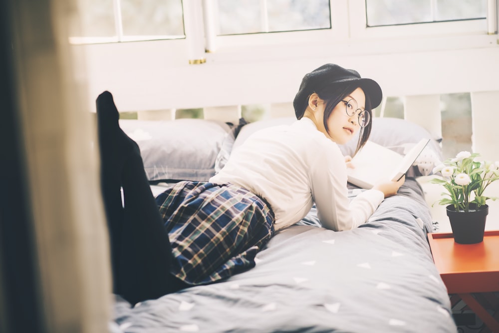 woman reading book while laying on bed