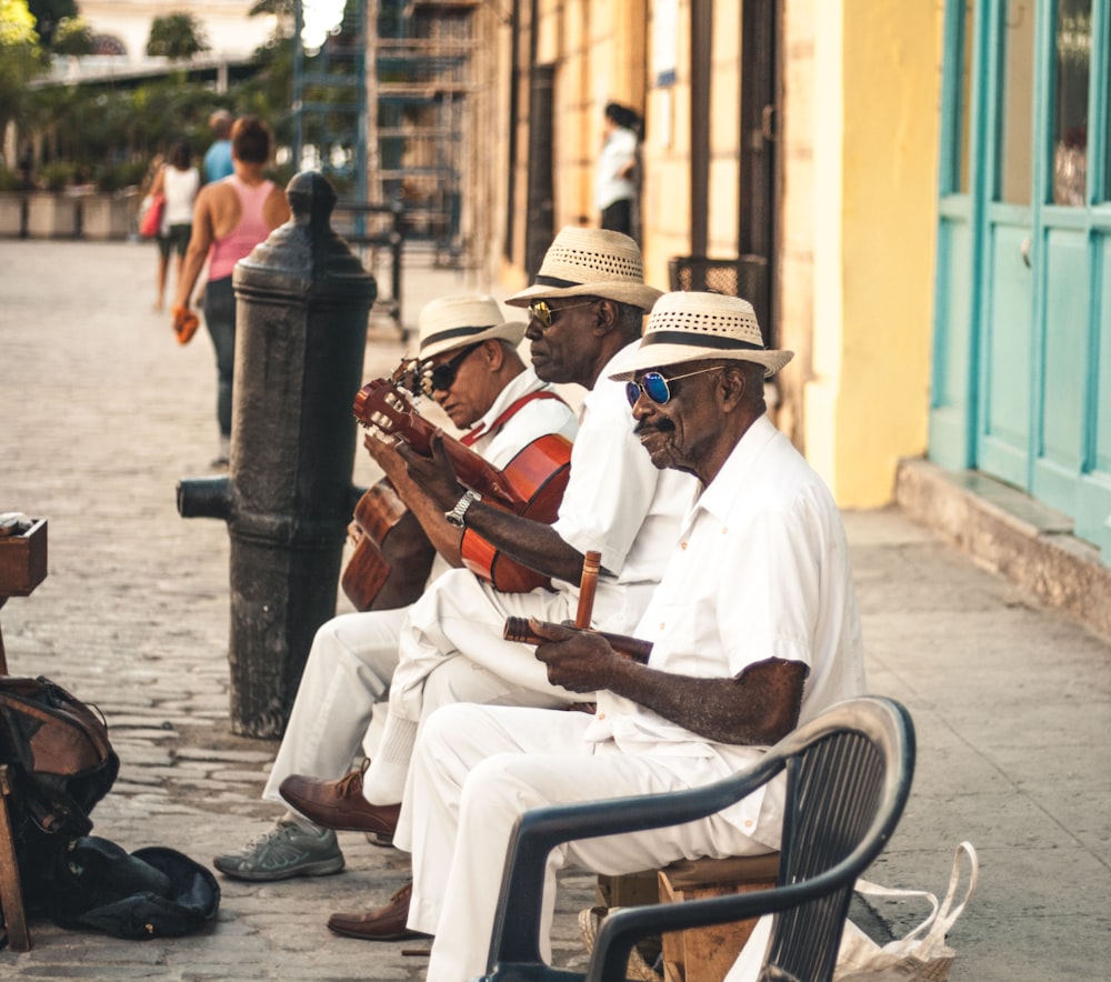 uomo che suona la chitarra acustica mentre si siede sulla panchina