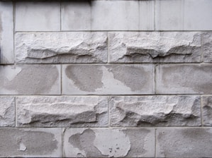 Rough textured stone blocks arranged in a horizontal pattern. The stones exhibit irregular shapes with a weathered appearance, featuring a mix of smooth and rugged surfaces.