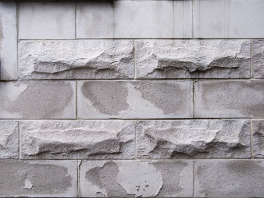 Rough textured stone blocks arranged in a horizontal pattern. The stones exhibit irregular shapes with a weathered appearance, featuring a mix of smooth and rugged surfaces.