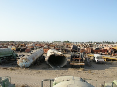 A large scrapyard filled with rusted and abandoned vehicles and machinery, including tankers, trucks, and other heavy equipment spread across a dusty, barren landscape.