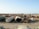 A large scrapyard filled with rusted and abandoned vehicles and machinery, including tankers, trucks, and other heavy equipment spread across a dusty, barren landscape.