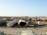 A large scrapyard filled with rusted and abandoned vehicles and machinery, including tankers, trucks, and other heavy equipment spread across a dusty, barren landscape.