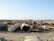 A large scrapyard filled with rusted and abandoned vehicles and machinery, including tankers, trucks, and other heavy equipment spread across a dusty, barren landscape.