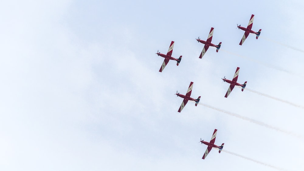 Six avions rouges sous un ciel blanc pendant la journée
