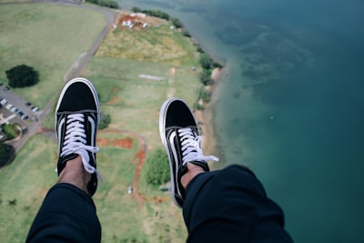 person wearing blue-and-white vans low-top sneakers with aerial view of body of water adventurous zoom background