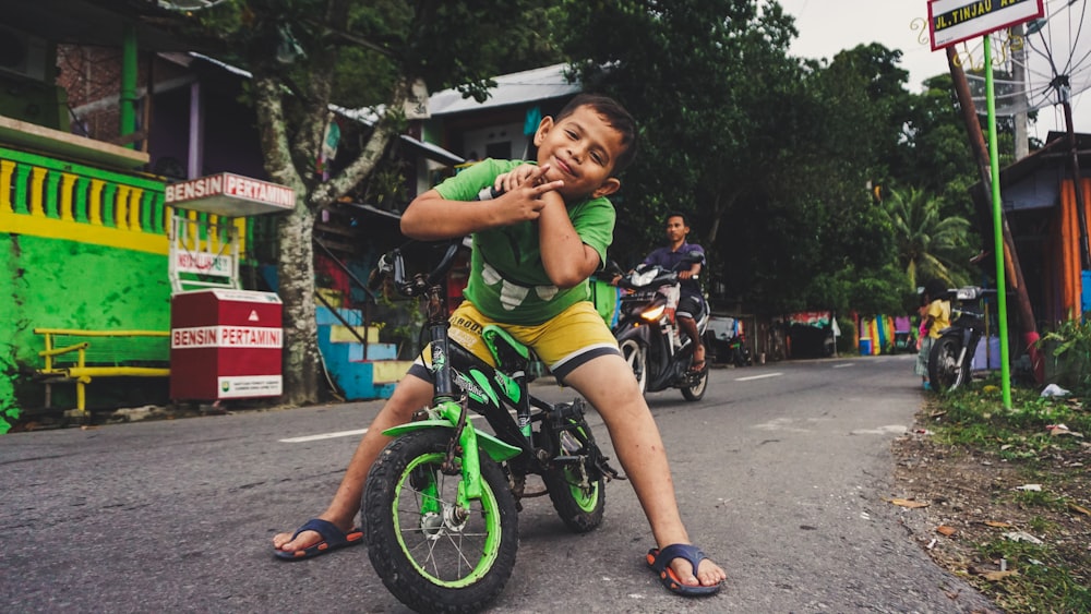 昼間にバイクに乗っている男の近くで黒と緑の自転車に乗っている男の子