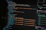 A close-up of a computer screen displays lines of HTML and CSS code. The code includes elements such as a navigation bar, container, and various task items with unique IDs. The screen also shows a styles section with properties like margin and padding.