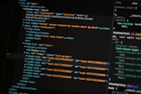 A close-up of a computer screen displays lines of HTML and CSS code. The code includes elements such as a navigation bar, container, and various task items with unique IDs. The screen also shows a styles section with properties like margin and padding.