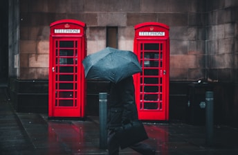 person under umbrella walking beside telephone booths