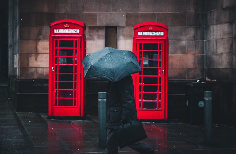 person under umbrella walking beside telephone booths