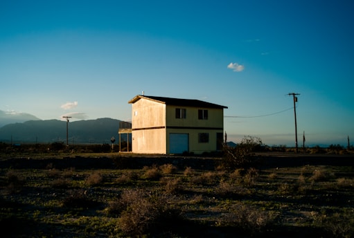 A sunlit desert homestead with solar panels and a thriving garden surrounded by rugged mountain terrain.