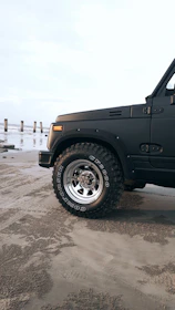Close-up of a rugged ATV tire leaving tracks on the golden beach sand at sunset.