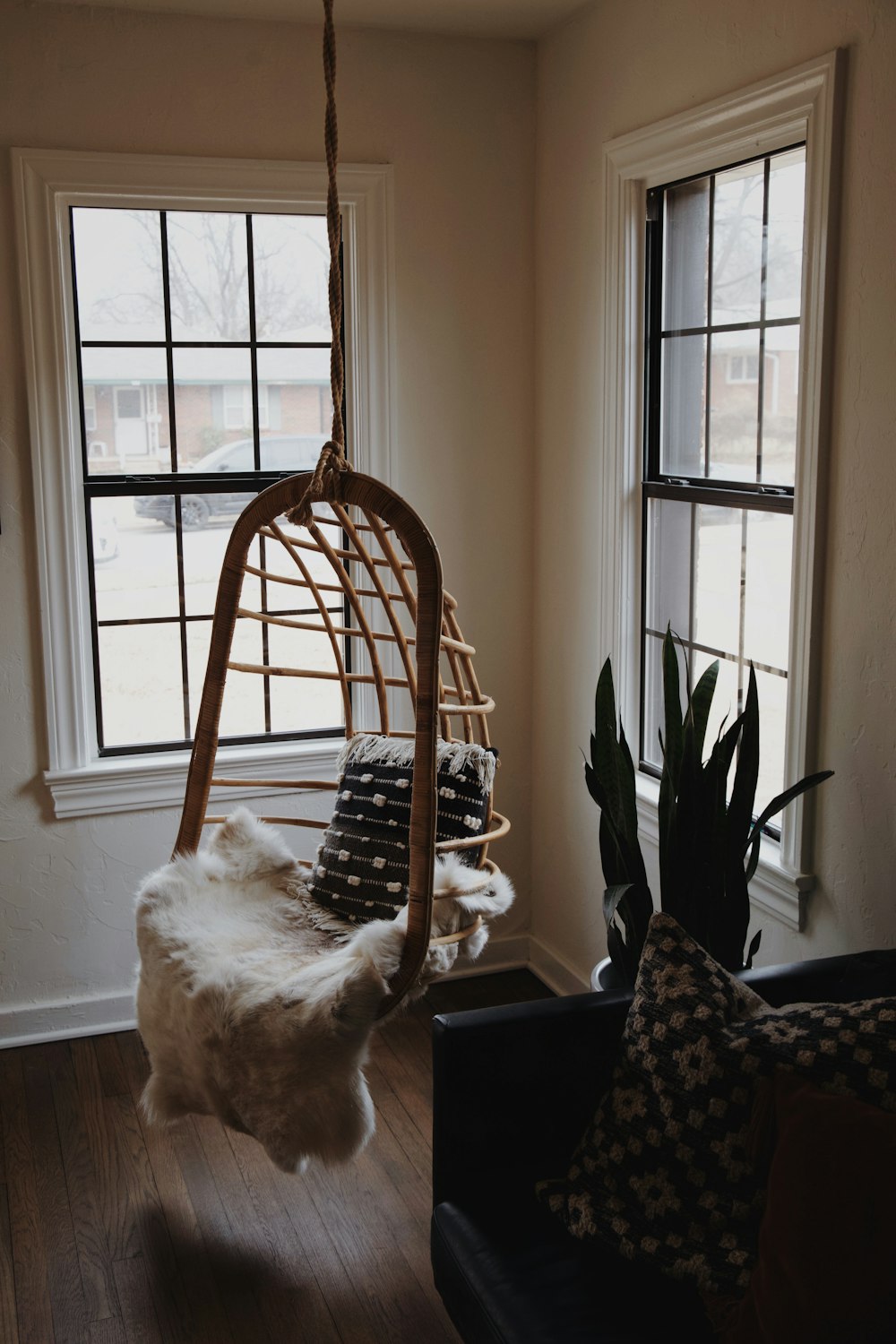 brown wooden hanging chair with white fleece blanket and gray throw pillow beside window during daytime