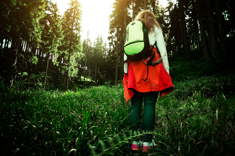 A hiker wearing the hypershell exoskeleton walking through a lush green forest trail with golden sunlight filtering through the trees.
