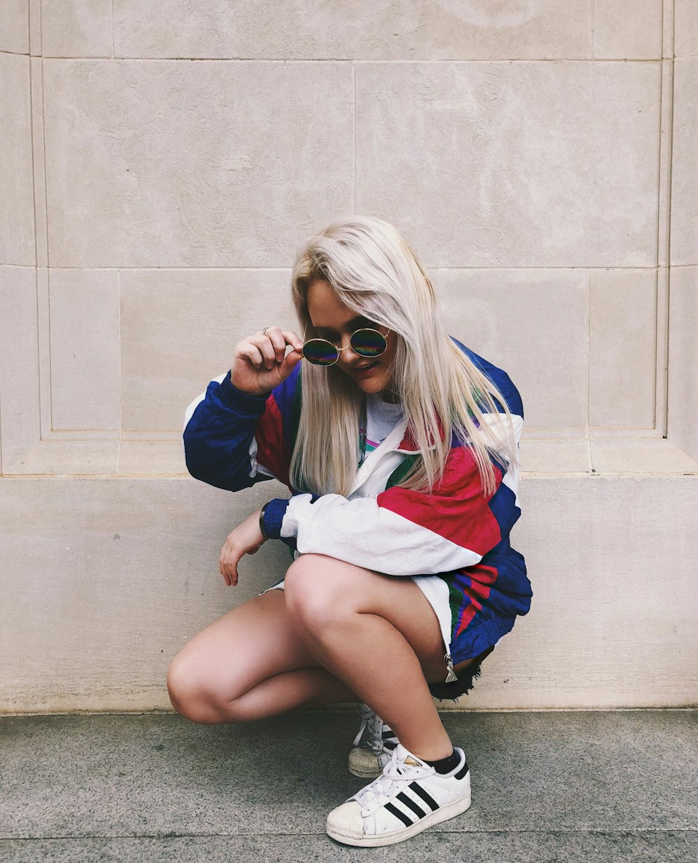 woman holding hippie sunglasses in front of beige painted wall